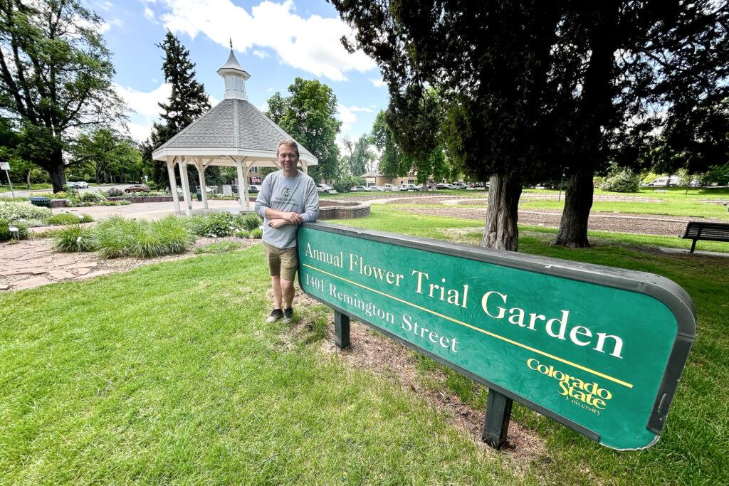 Chad Miller stands beside the green sign for the Colorado State University Annual Flower Trial Garden at 1401 Remington Street, with a white gazebo in the background.