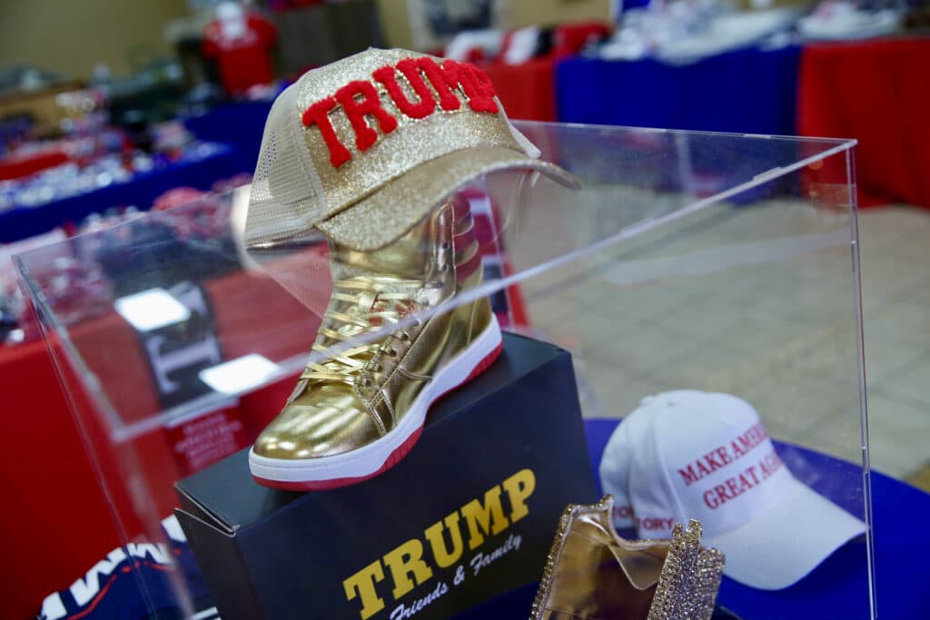 A golden hat that reads “Trump” is placed on top of a glass case showcasing a golden high-top sneaker.