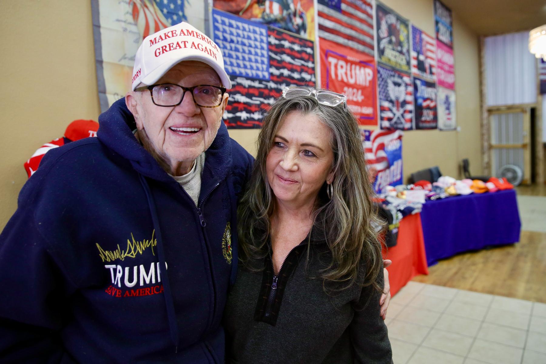 An older gentleman and a woman stand arm in arm.
