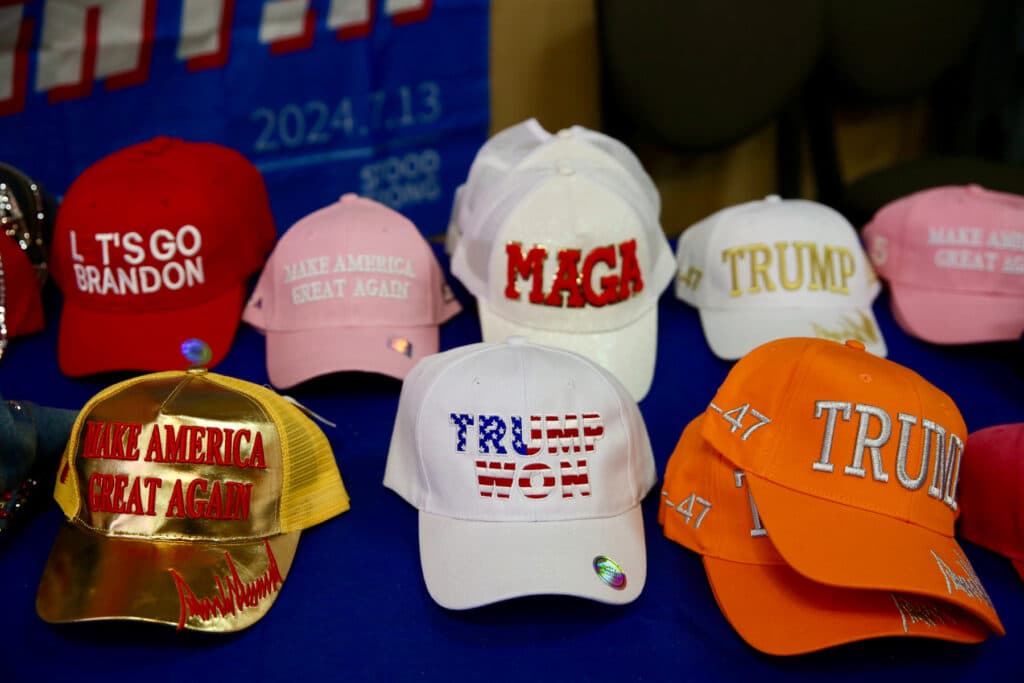 A selection of baseball caps with various Donald Trump-inspired slogans rests on a table.
