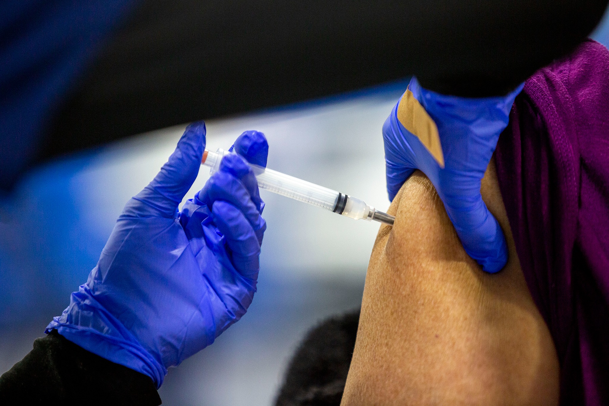 A gloved hand holding a shot going into the upper arm of a woman