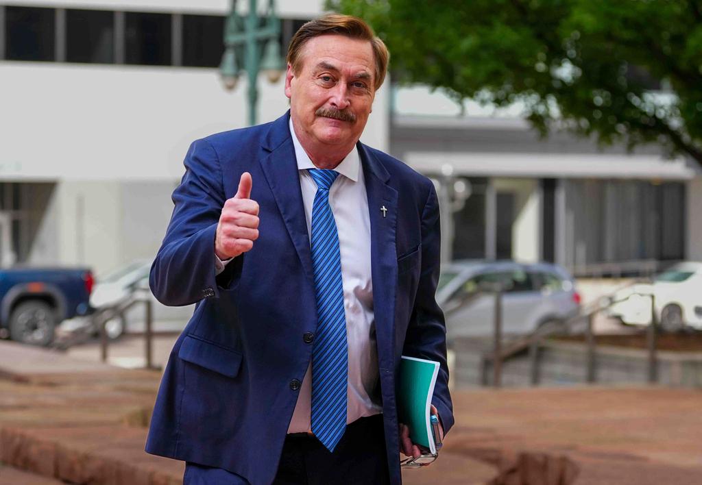 A man in a blue suit carrying a folder gives a thumbs up to the camera