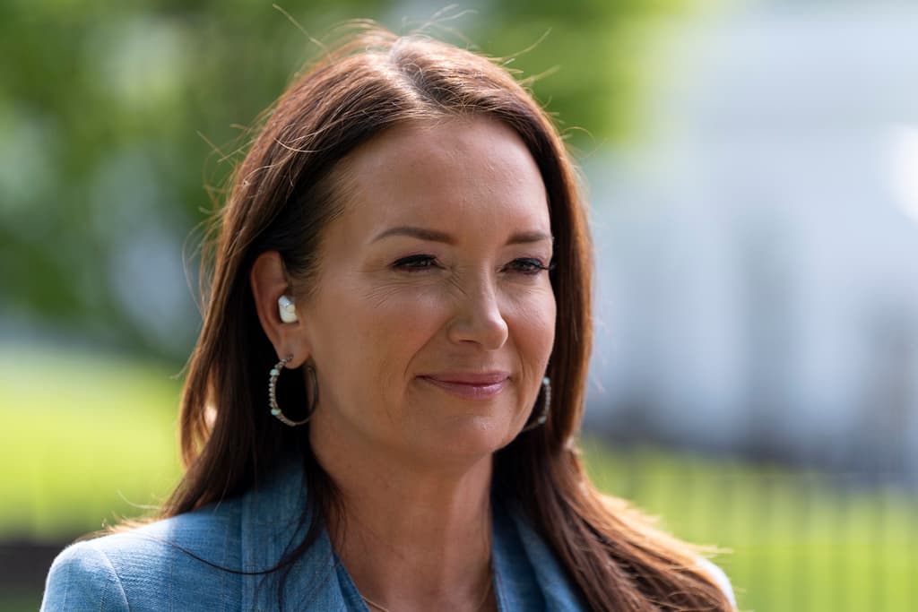 A woman wearing a blue shirt and earrings is smiling at the camera.