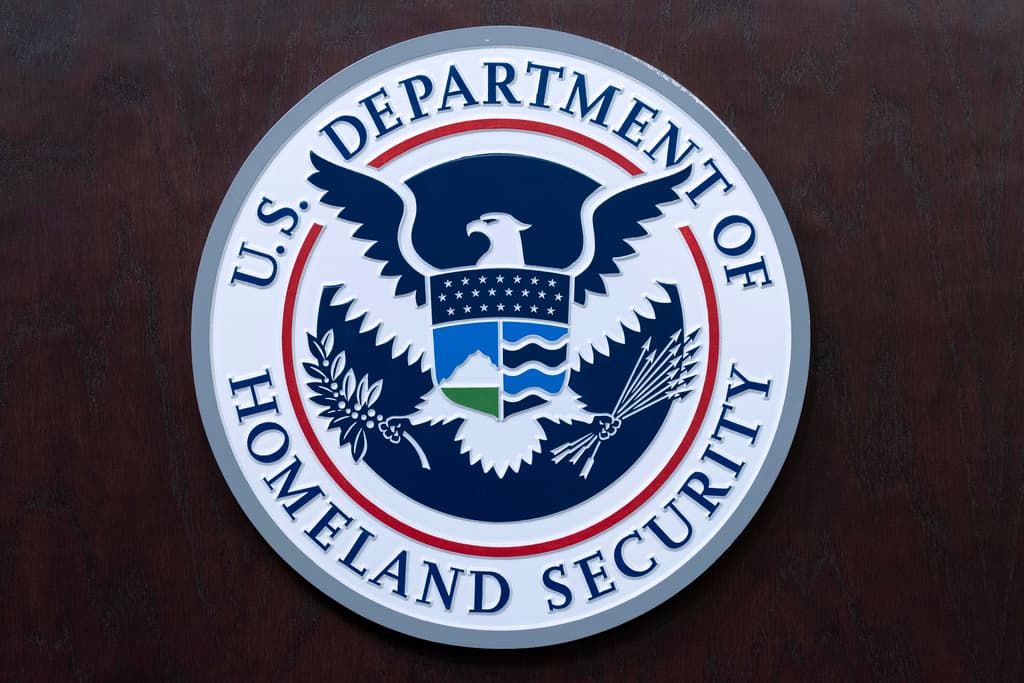The image features a circular logo for the United States Department of Homeland Security. The logo is blue and white, with a bird in the center.