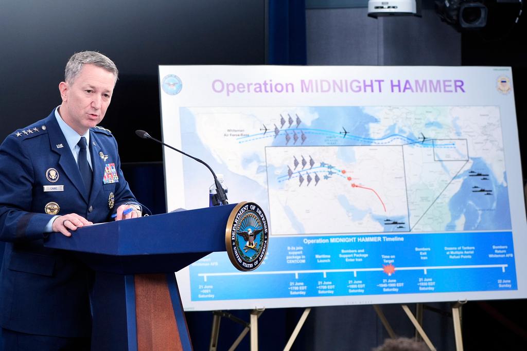 Man stands at podium with display board behind him.