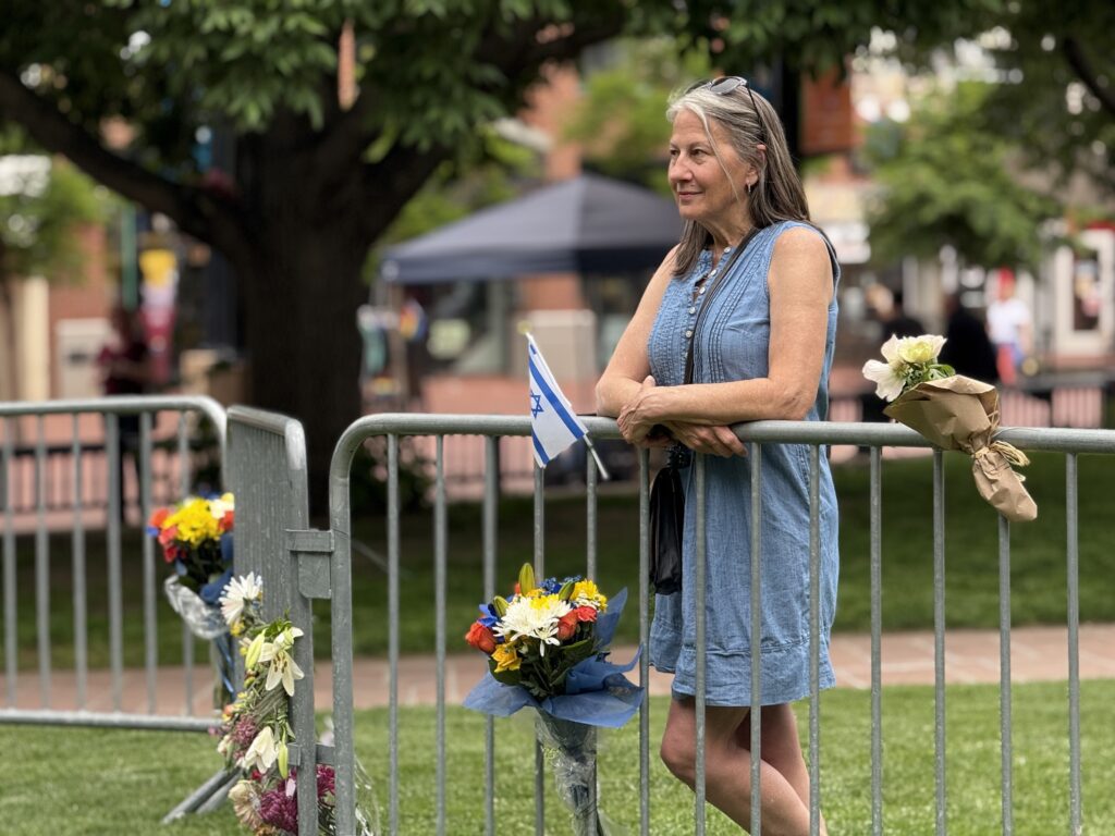 A woman in a blue dress stands holding a makeshift barrier that holds multi-colored flowers.