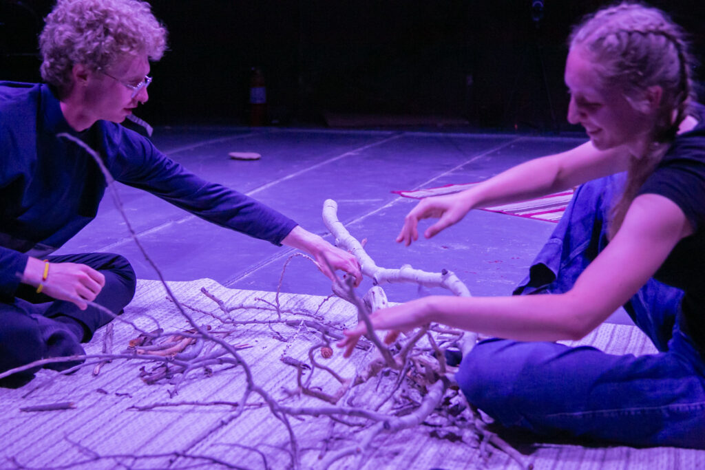 Asher Dobrin, left, and Holly McMahon, right, sit on a rug and break large sticks together.