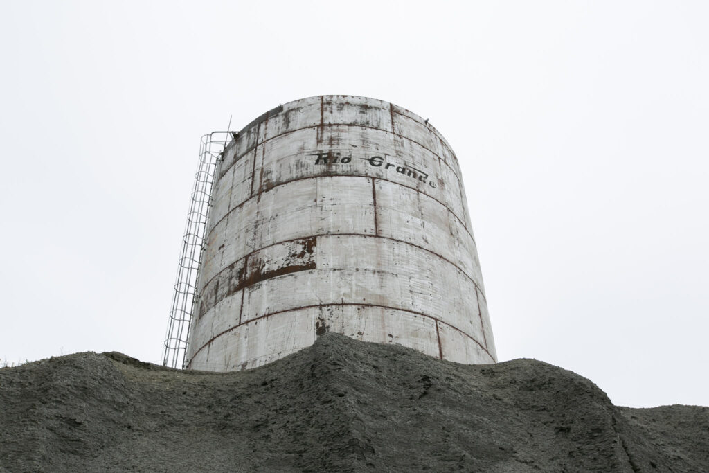 A large, corrugated metal water tank that reads "RIO GRANDE" sits atop a shale hill in Rangely, Colorado.