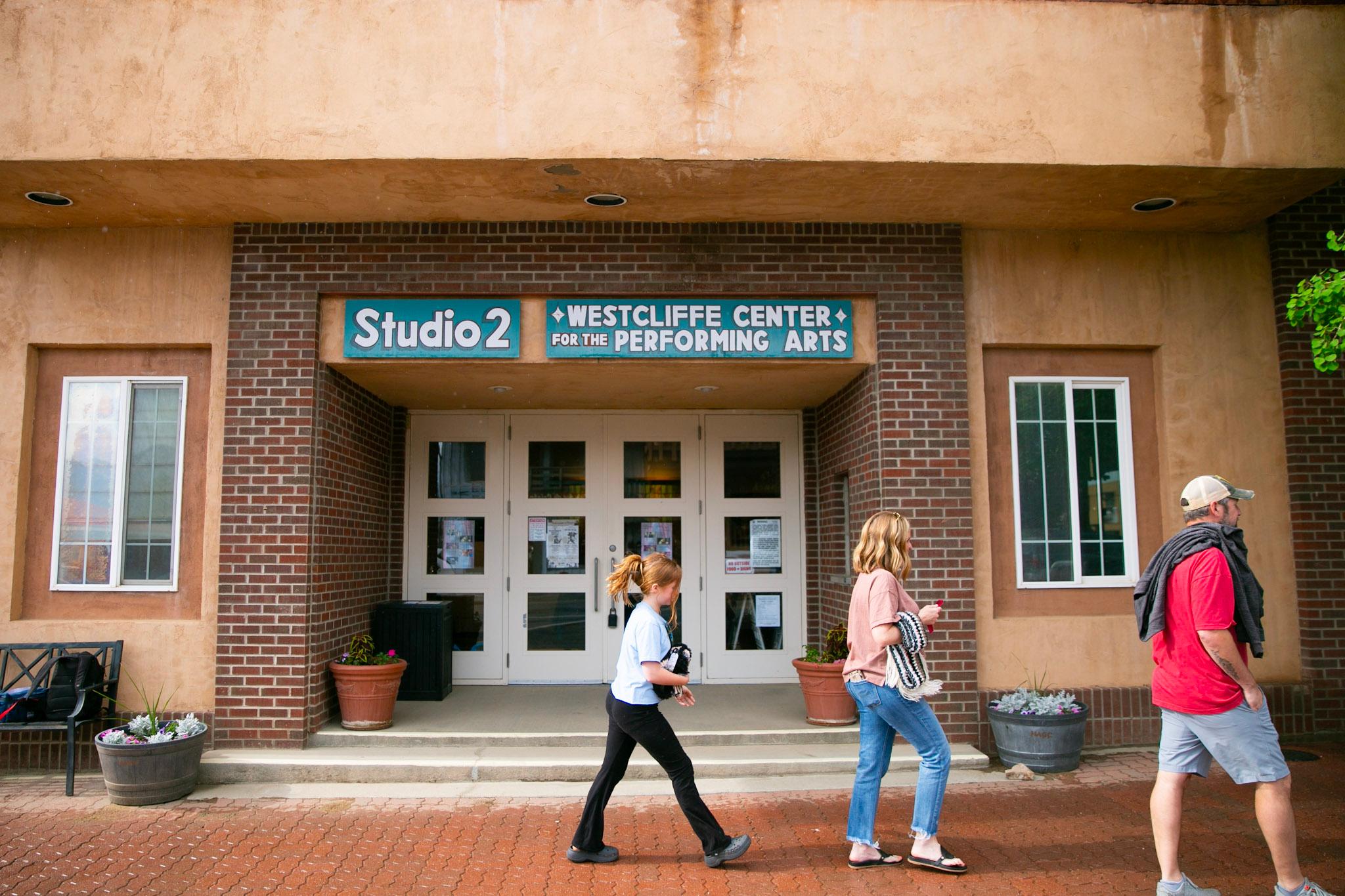 A family of three, mother father and a young girl, walk past the front of the Westcliffe Center for the Performing Arts.