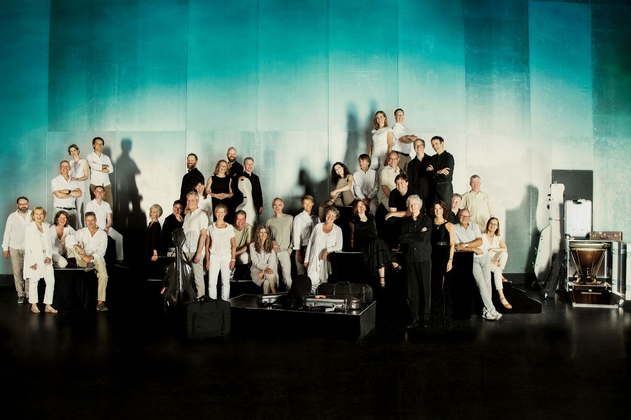 A group of classical musicians posing for a picture behind a grand piano.