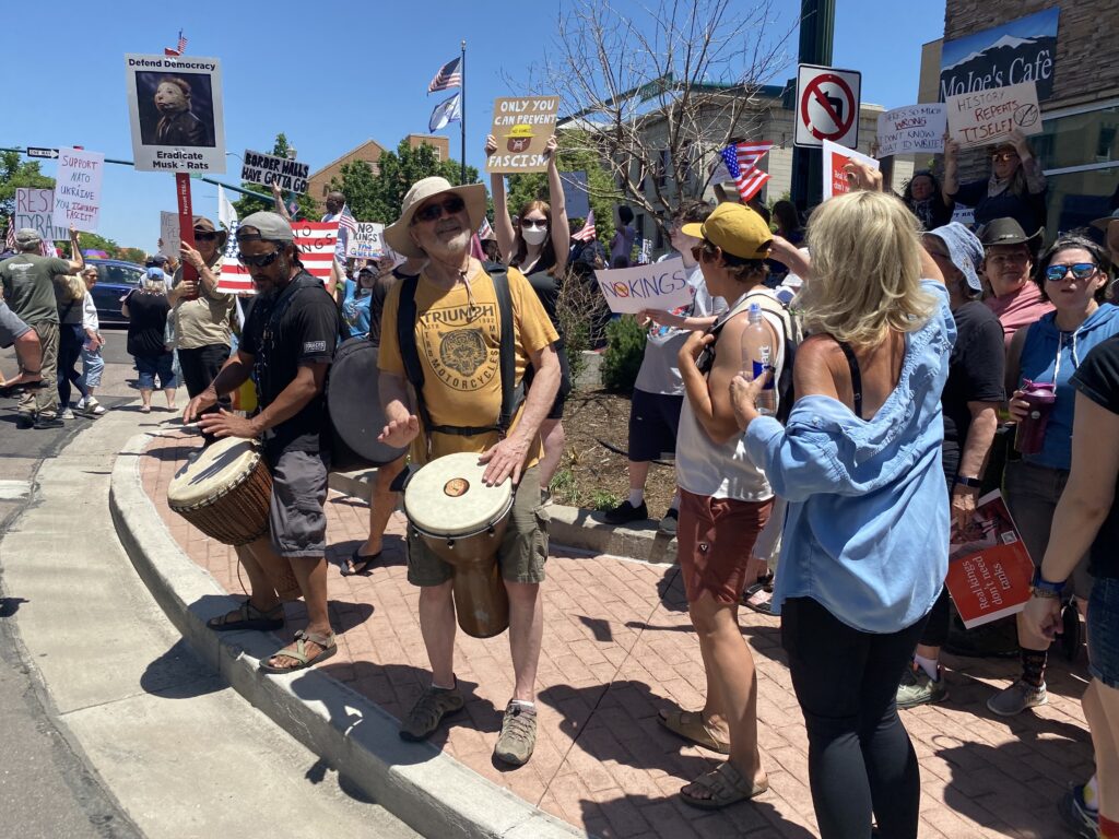 A group of people hold signs and bang drums on a sidewalk.