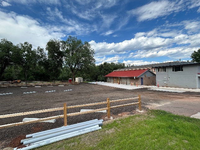 An empty dirt parking lot with two buildings on site.