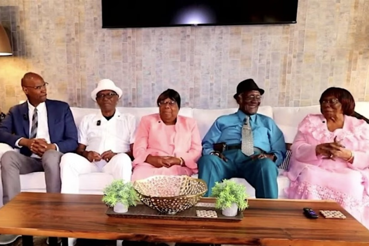 Five older black people sitting on a white couch, some smiling