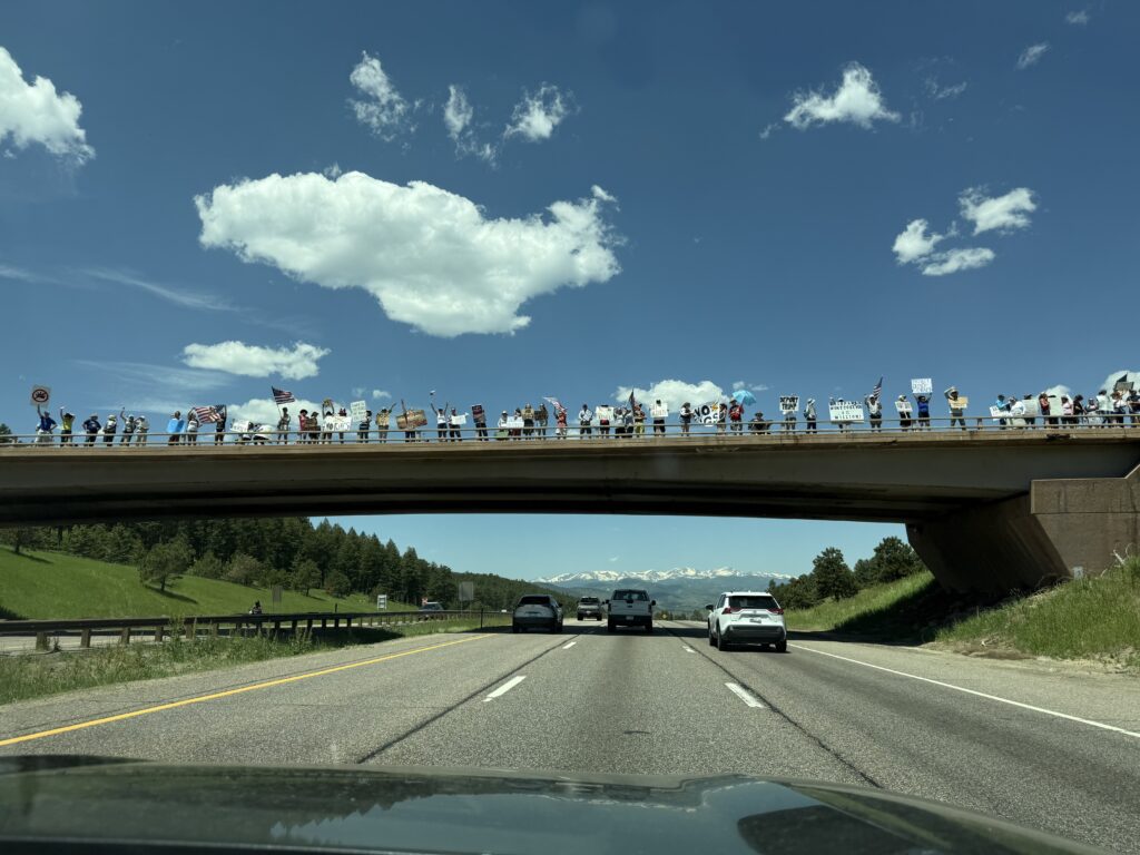 People stand on a bridge holding signs as a big white fluffy cloud hangs overhead.