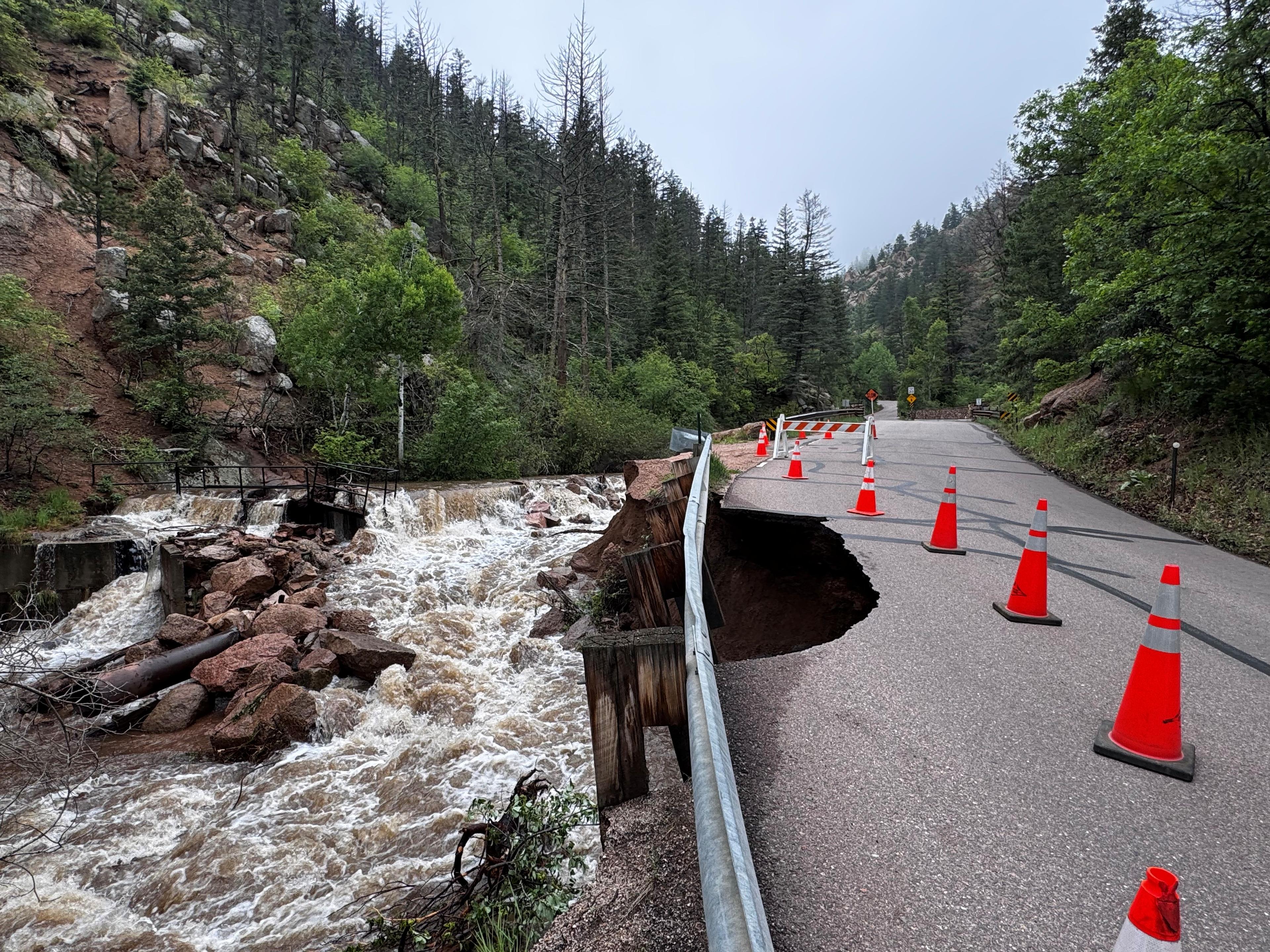 rushing waterway flows next to washed out road with orange cones