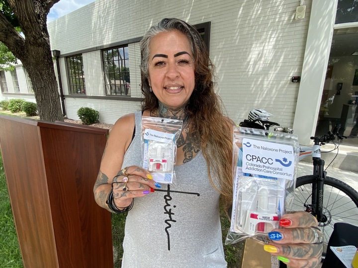 A woman in a gray tank-top t-shirt with the slogan "faith" holds naloxone kits designed to prevent overdoses