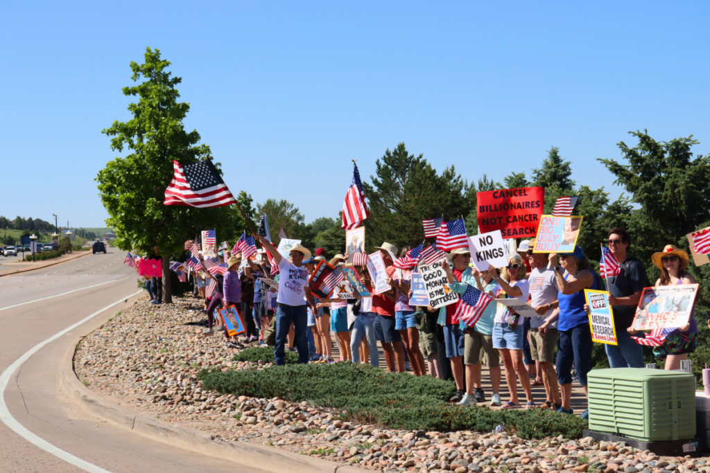 A large group of people are gathered on the side of a road, holding signs and flags.
