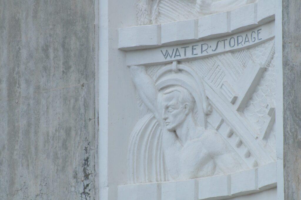 A white stone carving of a face and torso with the words water storage above