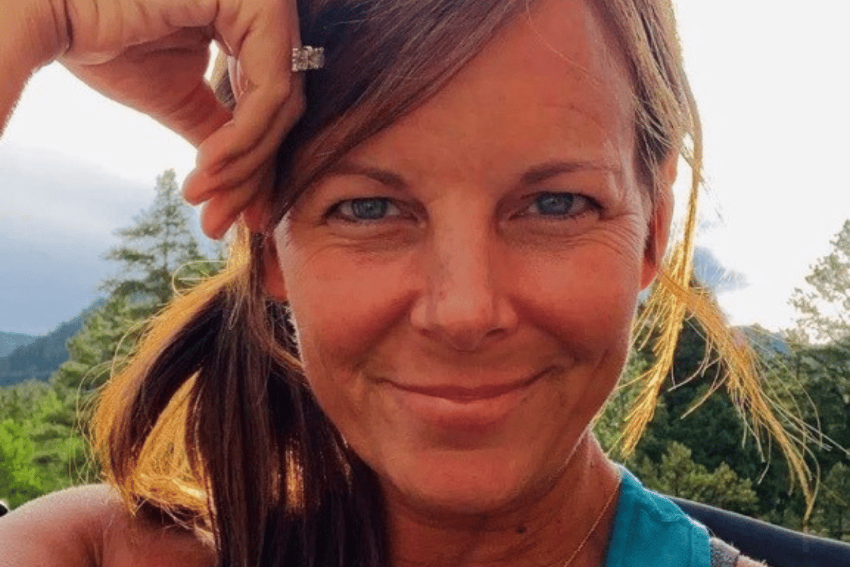 A woman with brown hair is smiling and wearing a ring on her finger. She is looking at the camera