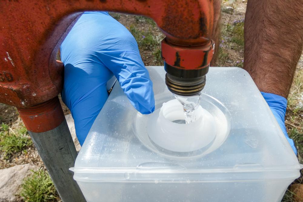 water flows from a pump into a plastic jug held by hands with latex gloves