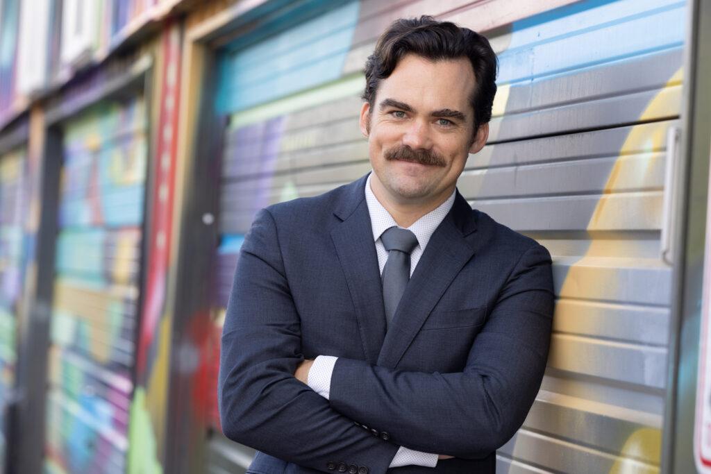 man with suit and mustache leaning against building
