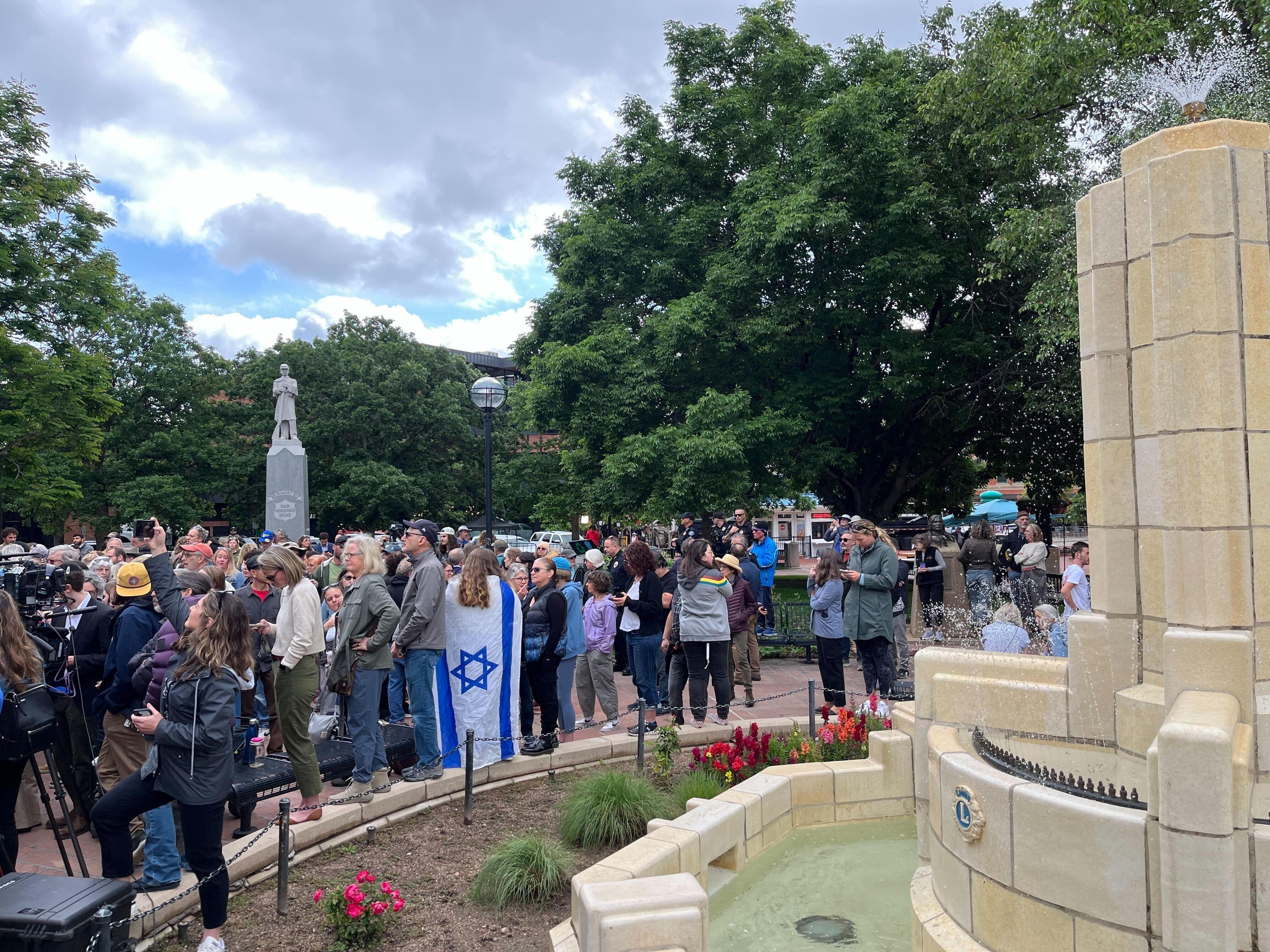 A large crowd of people stand on a brick sidewalk. Some hold the Israeli flag.