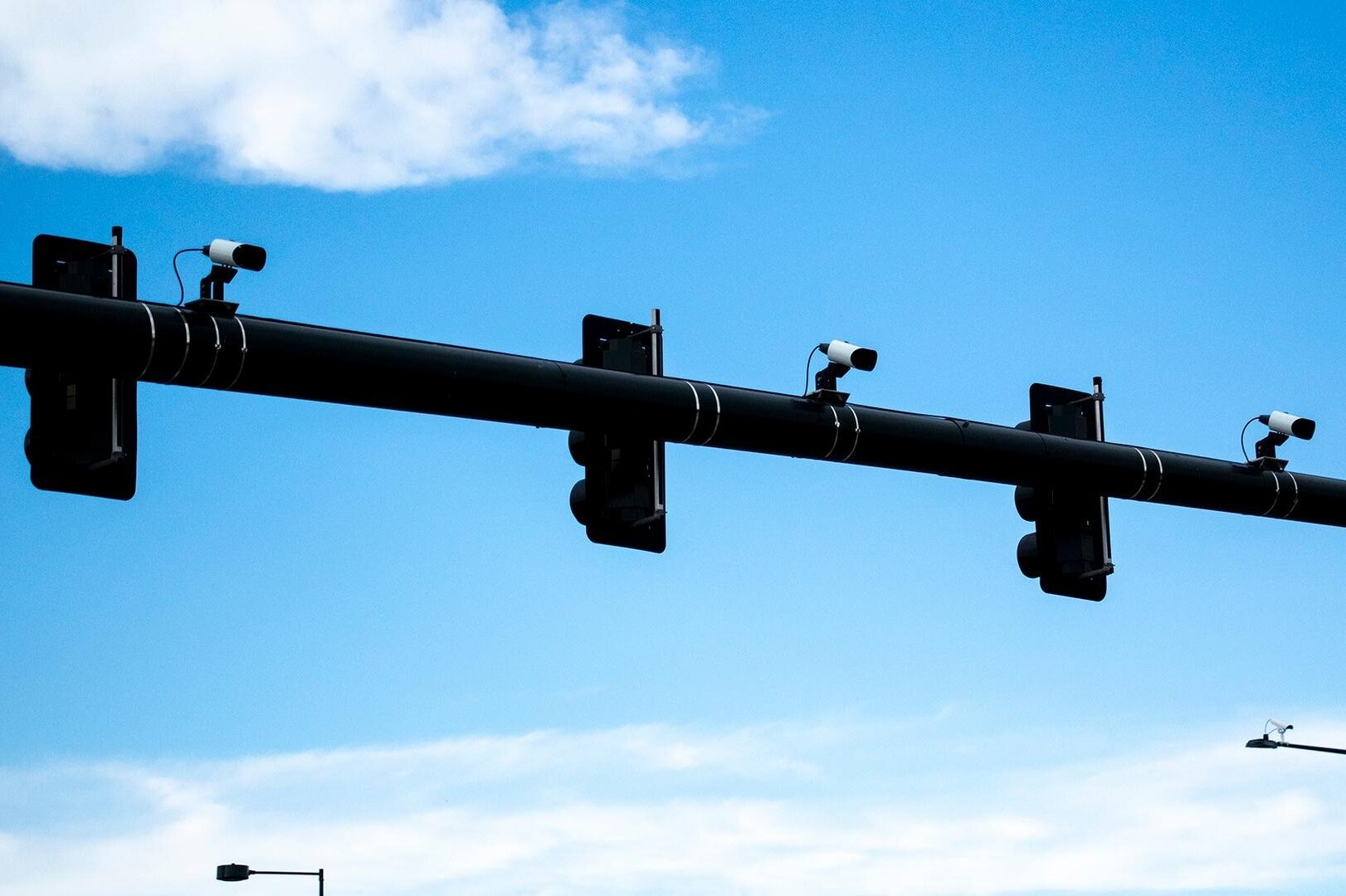 License plate-reading cameras attached to the top of a traffic signal witha a blue sky behind.