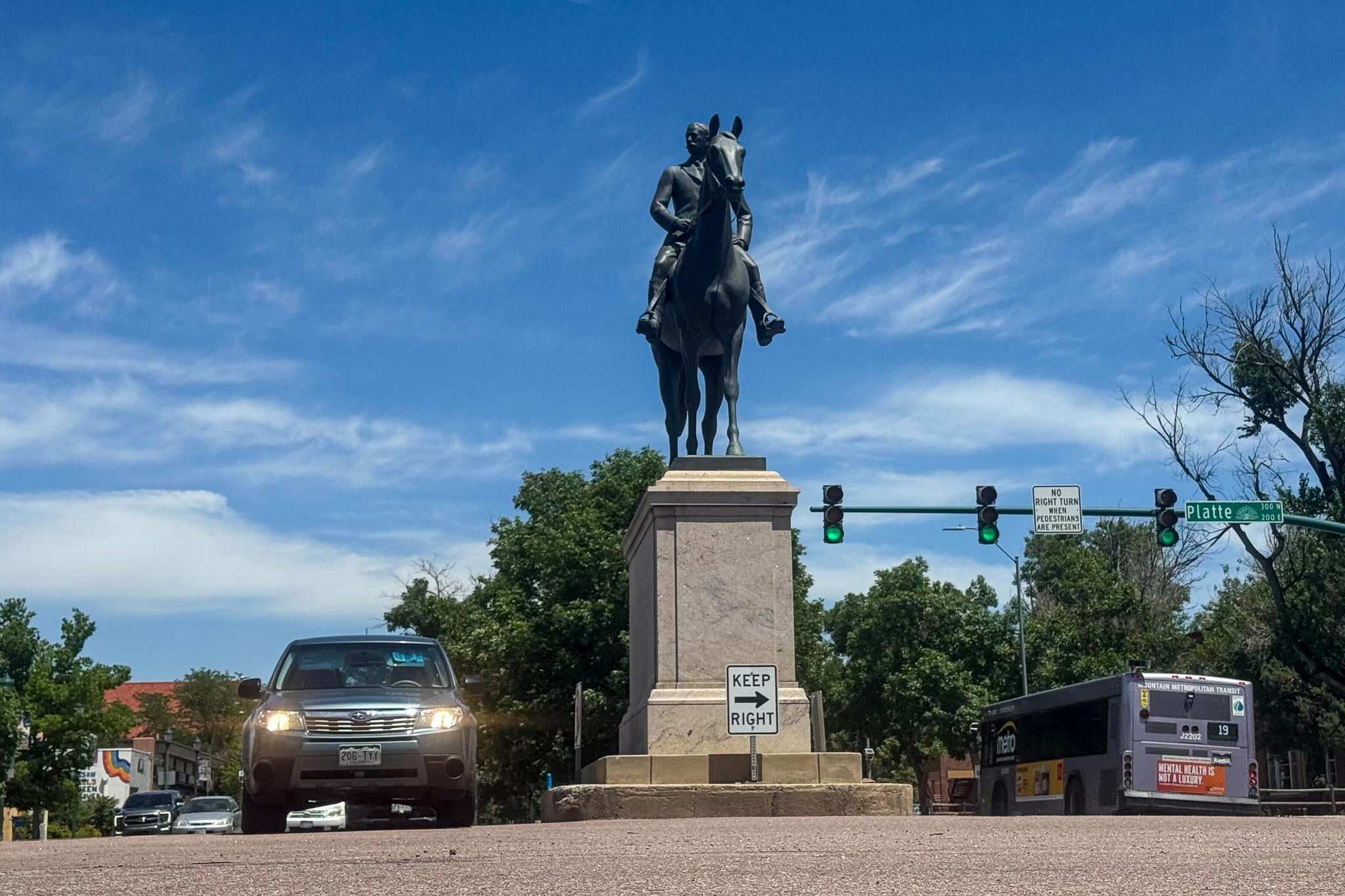 A statue of Colorado Springs’ founder on a horse sits smack in the middle of Nevada and Platte Avenues downtown, June 30, 2025. A bus and car pass by.