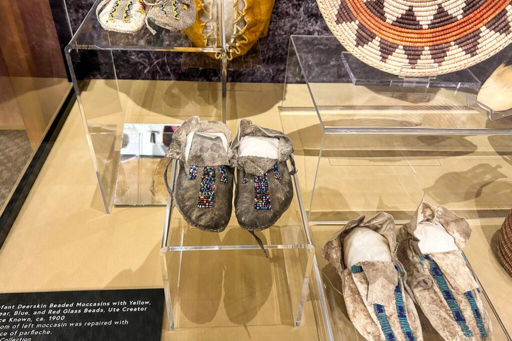 Photo shows moccasins and a basket on display at the Pioneers Museum in Colorado Springs elevating Ute culture and history.
