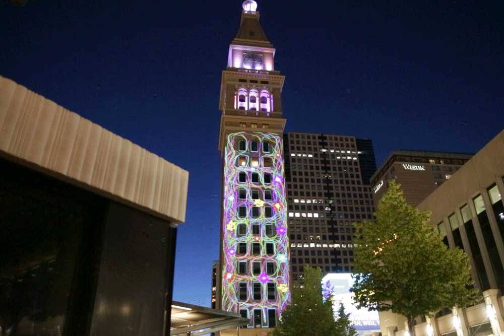A projection of a nodding monster fading in and out of cyber-vines on the Daniels and Fisher clocktower in Denver.