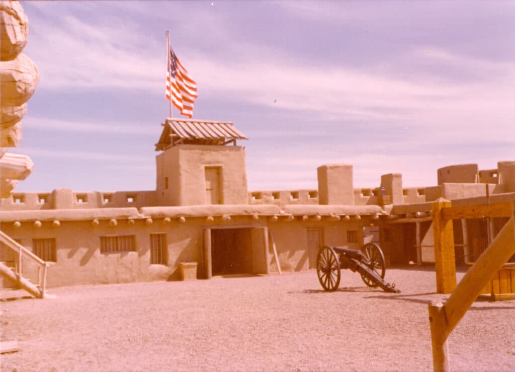 one story adobe fort with tower and american flag. A cannon is in the courtyard