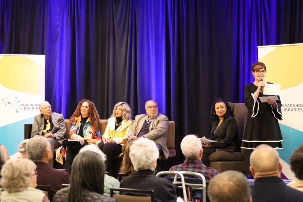 Photo shows four people seated next to a moderator in front of a dark purple curtain.