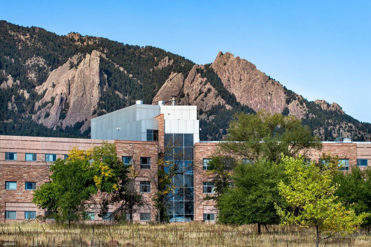 A large brick building with a mountain in the background. The building has a lot of windows and a large brick wall.
