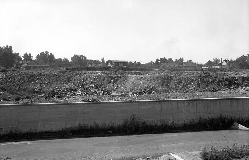Historic black and white photo shows a field of dirt and debris behind a short cement wall.