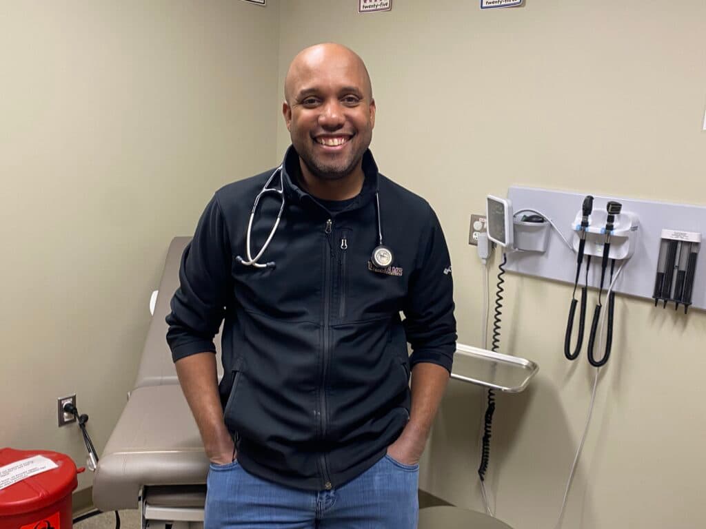 A Black doctor smiles in an examine room.