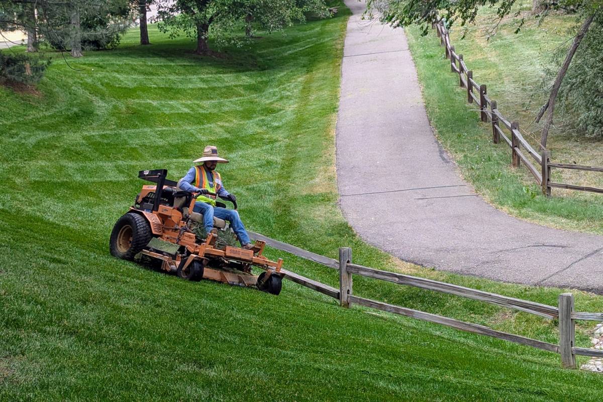 A landscaper operates a lawnmower on a hillside