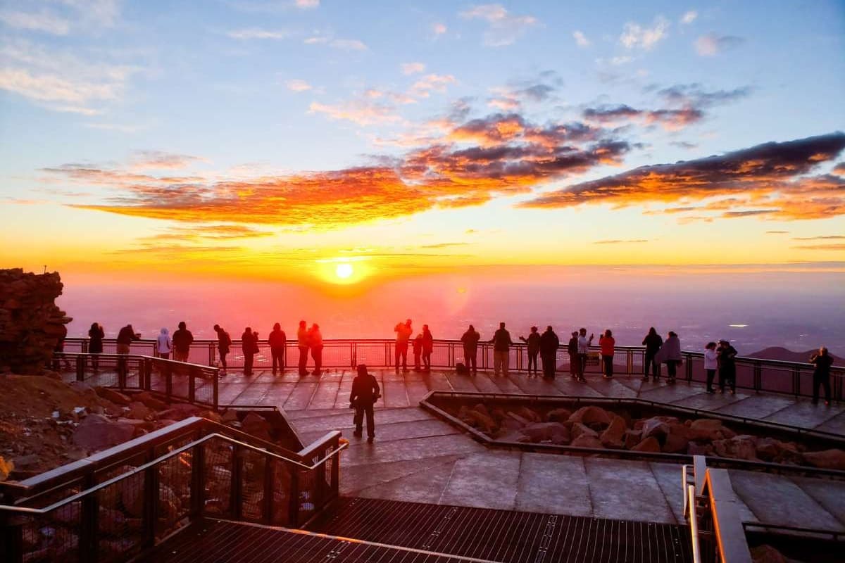 A crowd of people standing at the edge of Pikes Peak during sunrise.