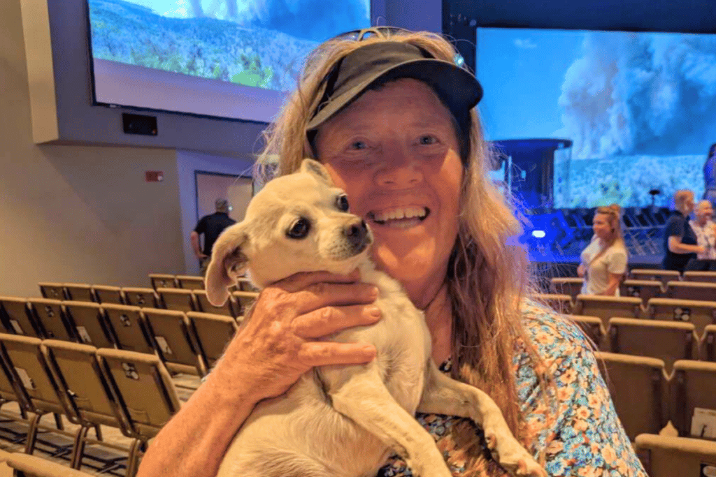 Woman in a visor holding a small cream colored dog smiling at the camera