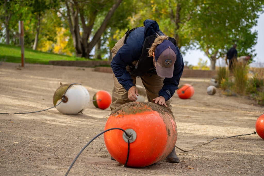 A person wearing a jacket and hat bends over a buoys