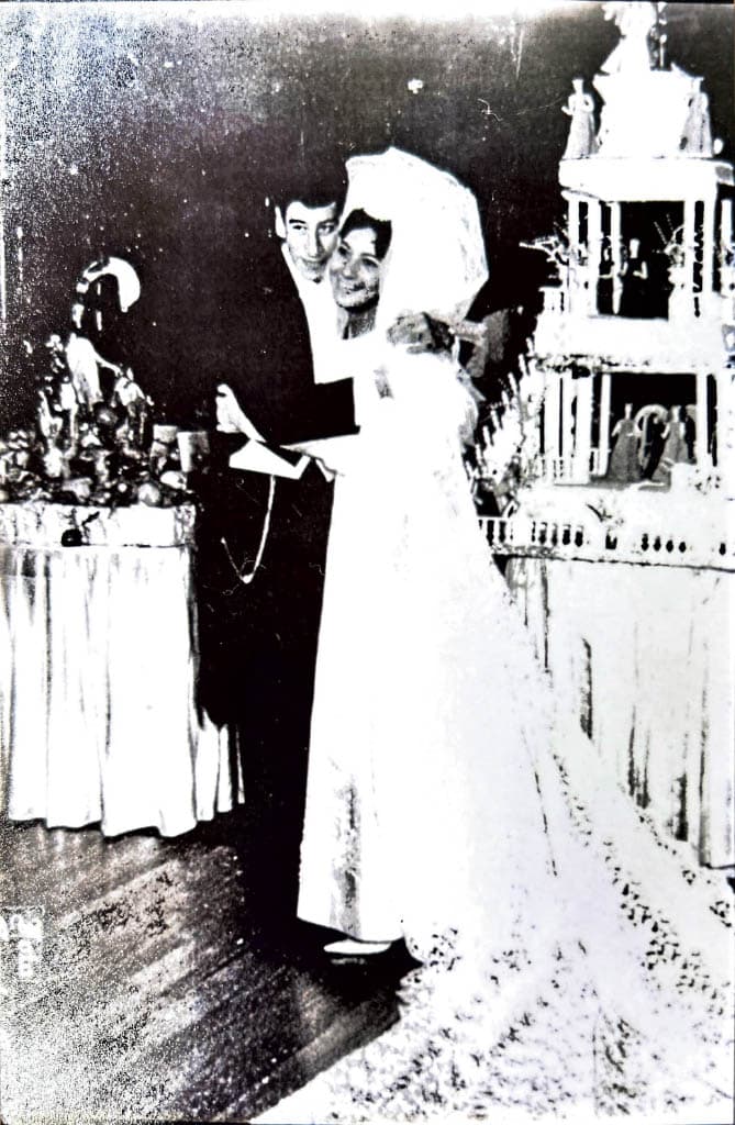 Black-and-white photo of the bride and groom smiling together, with a decorated wedding cake visible in the background.