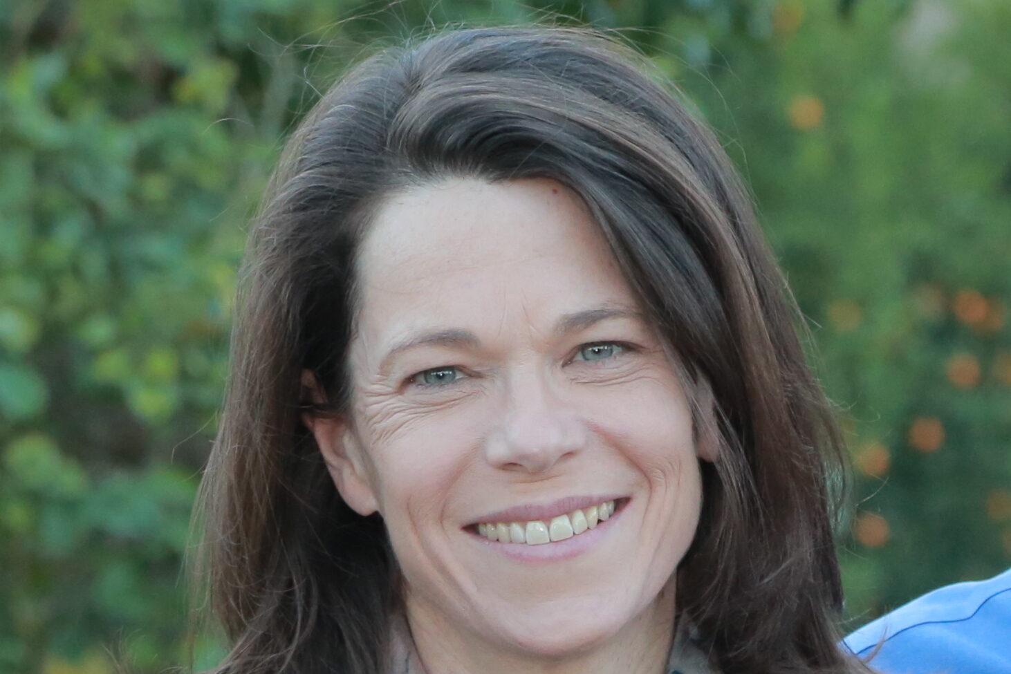 Image of a woman's face and she is smiling. She has short brown hair