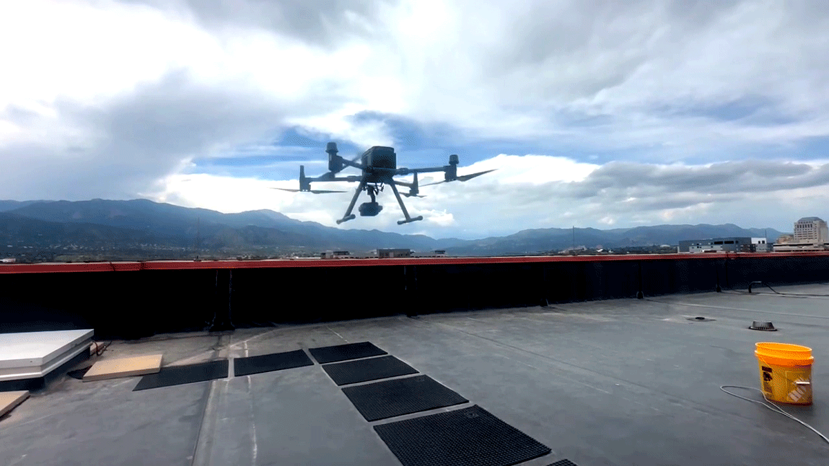 This animated gif depicts a drone hovering in the air on a rooftop.