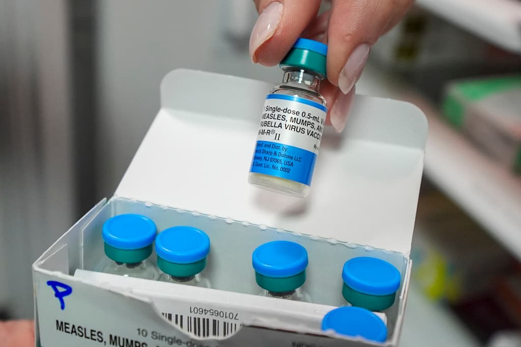 A hand holds a vial out of a box of vials with blue tops