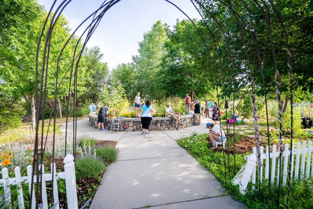 Several people in a garden with a white picket fence surrounding it