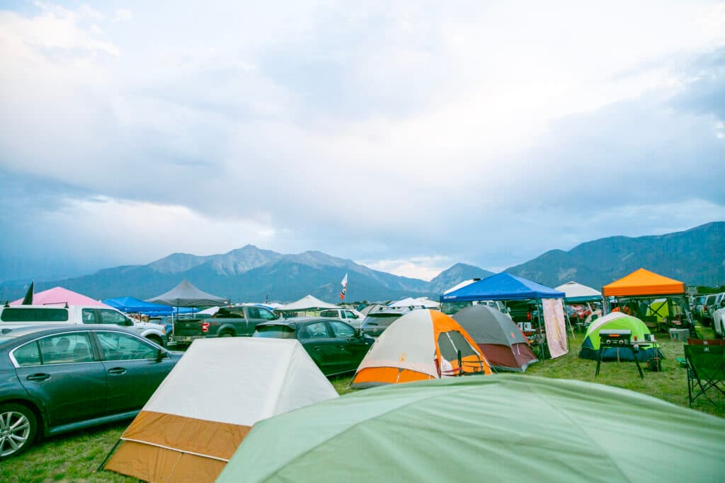 A field full of tents and cars sit up against a wall of tall peaks.