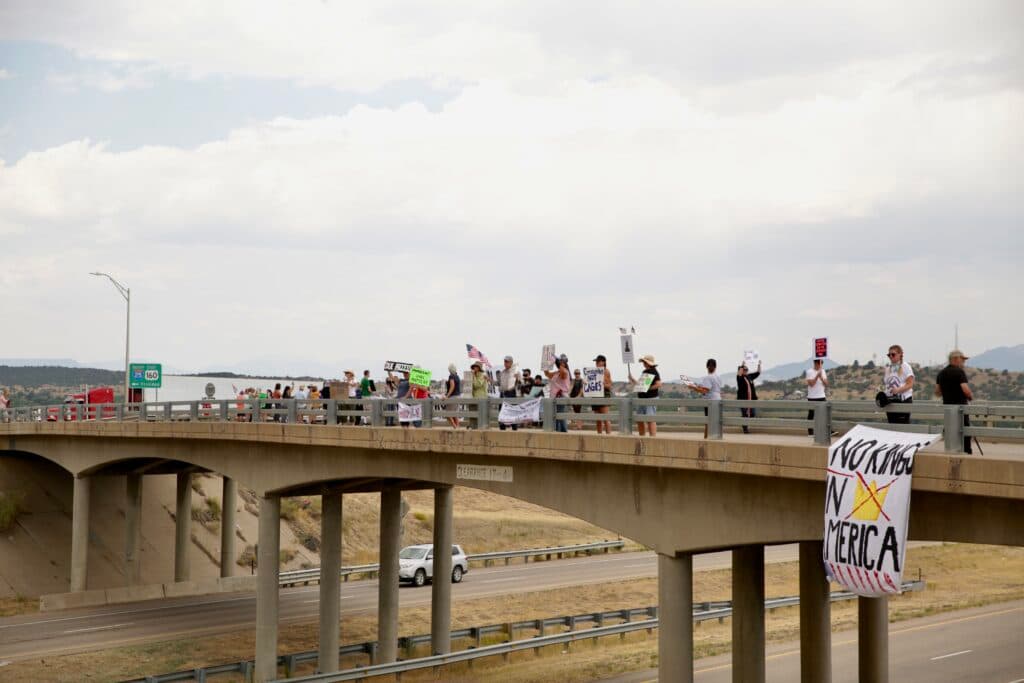 Protesters carrying signs line a bridge over a highway in Walsenburg