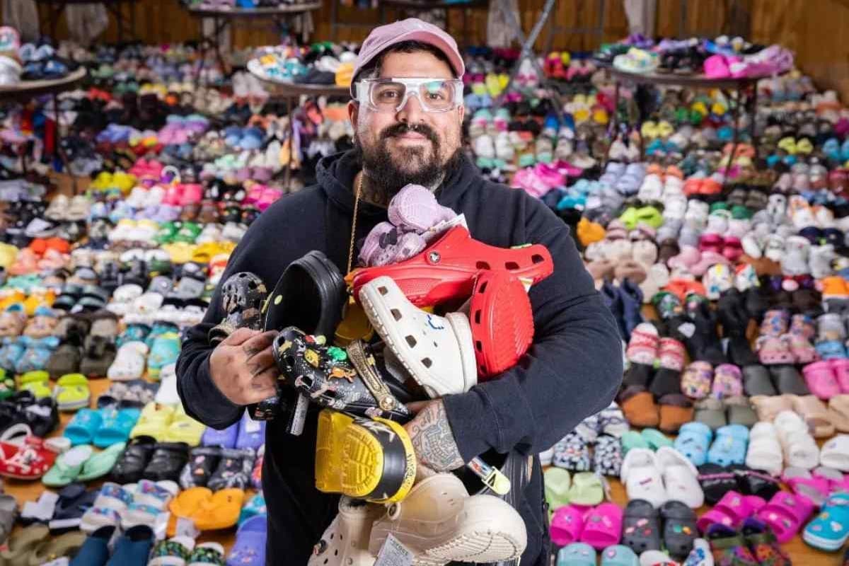 A man holds a pair of croc shoes surrounded by crocs