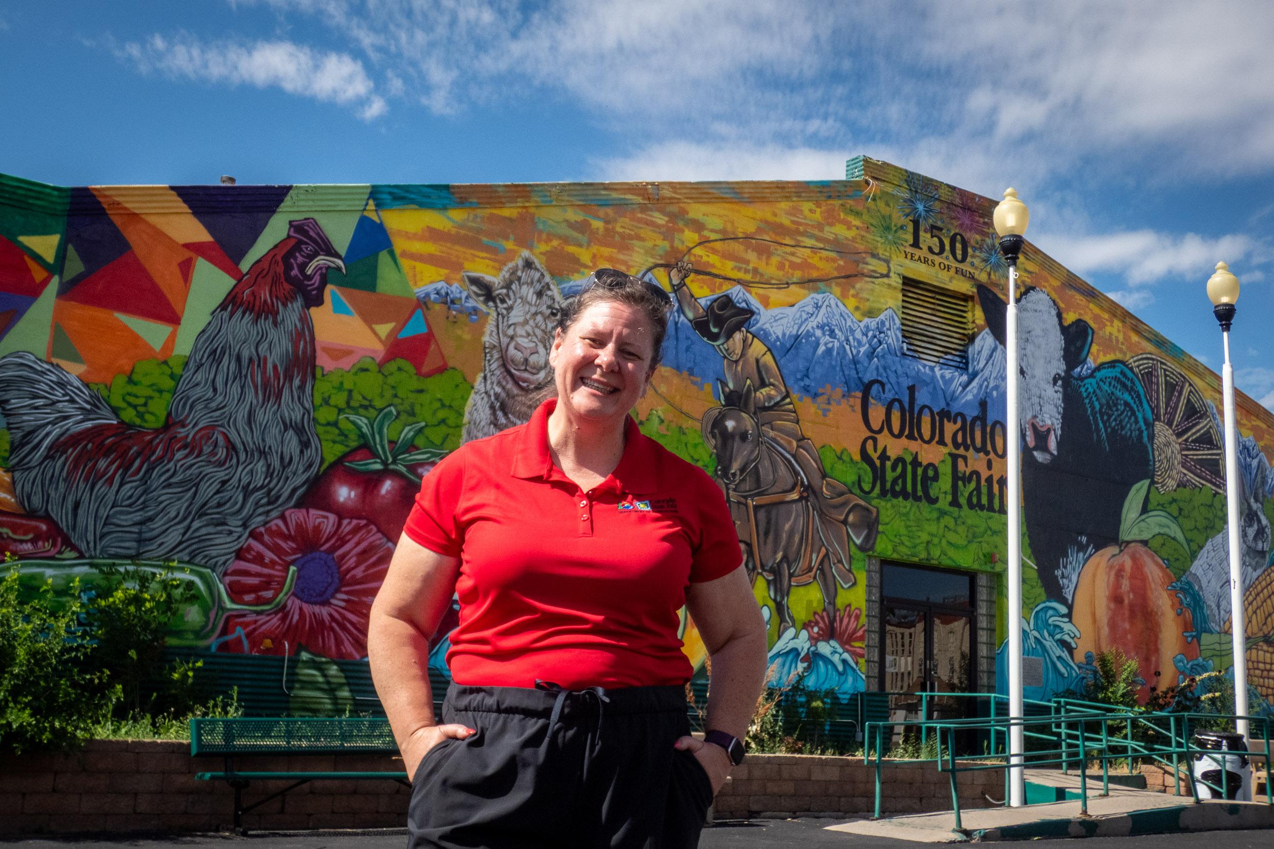 person stands in front of building painted with colorful mural depicting farm and ranch scenes and animals