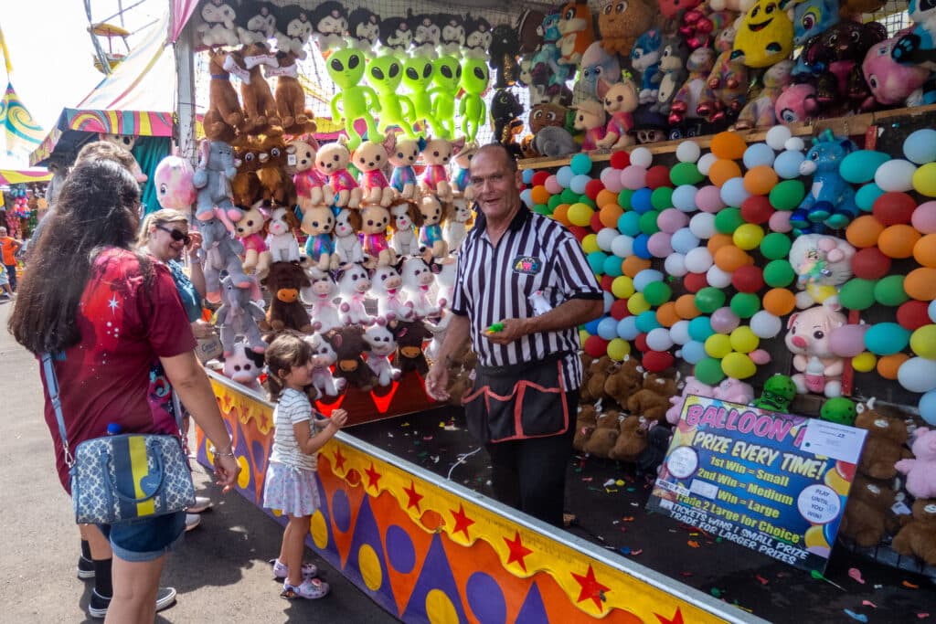a family stands at carnival booth filled with balloons and plush toys