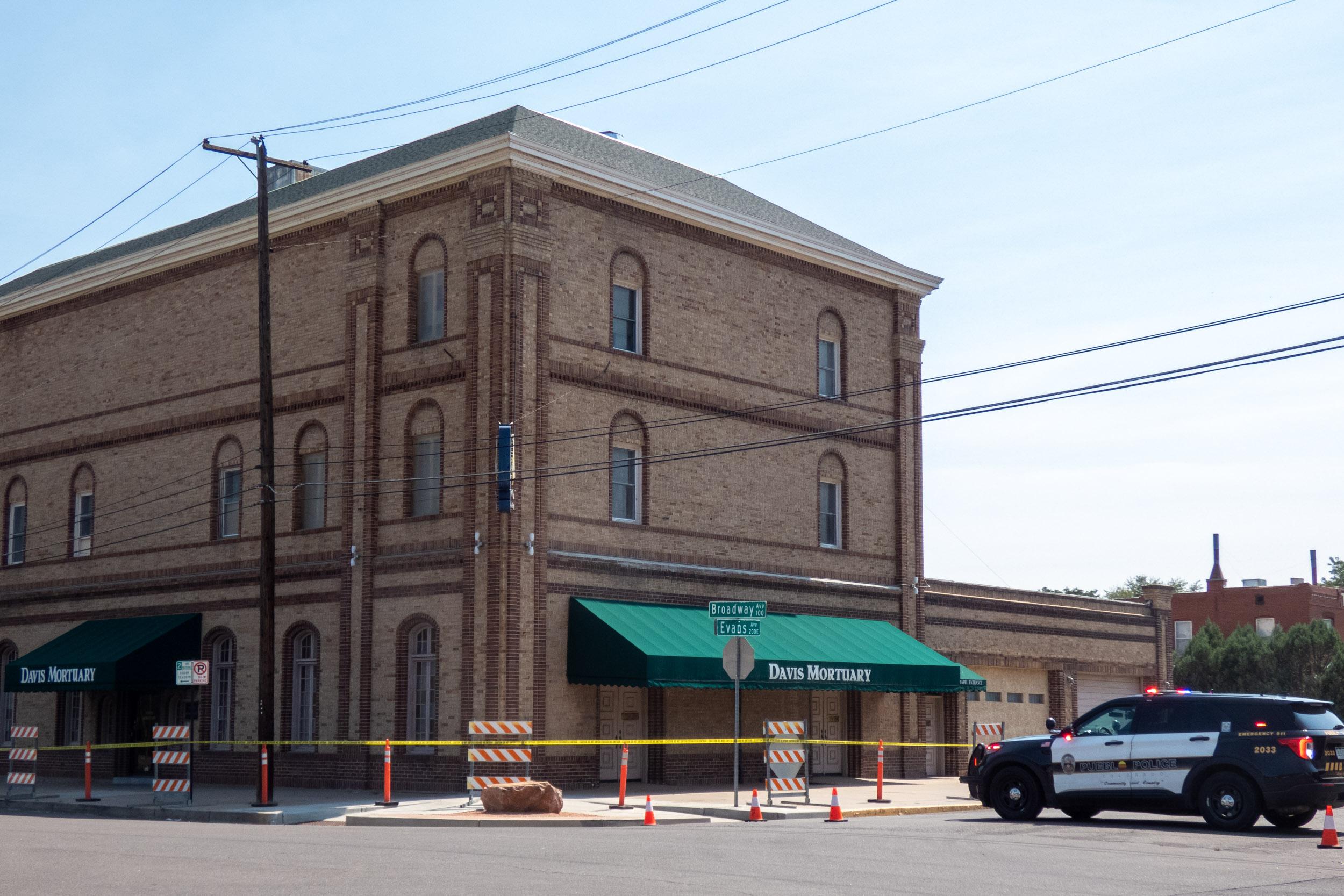 three story brick building with green awnings surrounded police tape and barriers